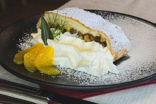 Warmer Apfelstrudel mit Puderzucker, Vanillesauce und Früchten auf einem Teller angerichtet